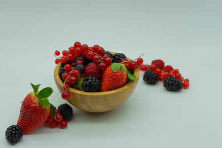 Close up view of a wooden bowl with strawberries, raspberries, blueberries, red currants and...