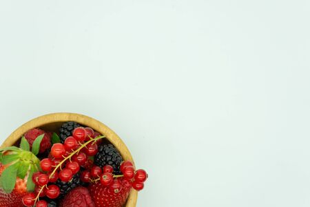 View of a wooden bowl filled with strawberries, blackberries, raspberries, redcurrants and...