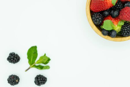 Top view of a wooden bowl filled with strawberries, blackberries, raspberries and blueberries in the upper right corner with fruit on the outside. White background, space for text. Healthy food concept, fruits of forest.の写真素材
