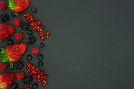 Black background with currants, blueberries, strawberries, raspberries and blackberries on the left side of the image with space for text on the right. Healthy food concept. Fruits of the forest.の写真素材
