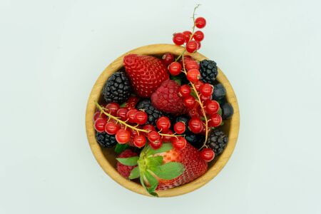 View of a wooden bowl filled with strawberries, blackberries, raspberries, redcurrants and blueberries. White background. Healthy food concept, fruits of the forest.の写真素材