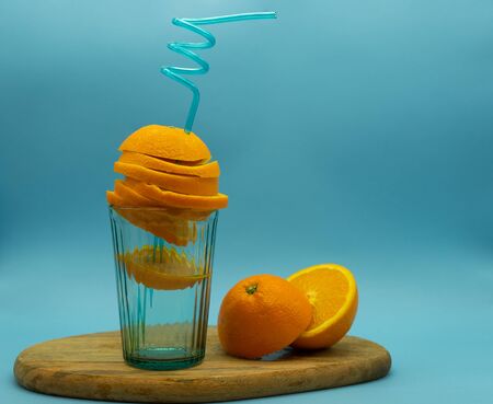 Orange crossed with a straw inside a glass on a wooden board with oranges around it, isolated on a...