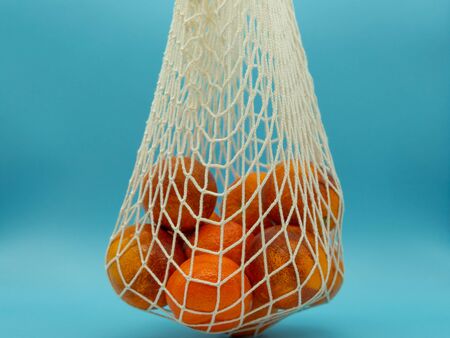 Organic cotton bag full of oranges held in a blue background. Citrus fruit. Zero waste concept.