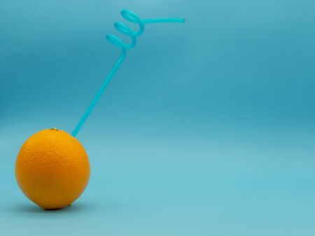Orange with blue curved straw on the left side of the image, isolated on a blue background. Citrus...