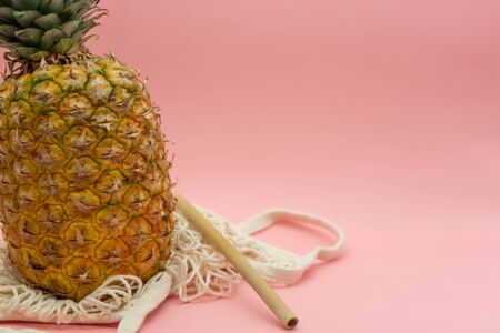 Pineapple with organic cotton bag and isolated bamboo straw on a pink background, located on the left of the image with space for text on the right. Tropical fruit. Healthy and ecological food concept. Zero waste.の写真素材