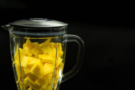 Blender filled with isolated pineapple on a black background on the left of the image with space for text on the right. Tropical fruit. Healthy food concept.の写真素材