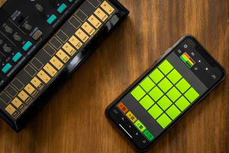 Top view of fm synthesizer and smartphone with drum machine application on a wooden table Electronic music concept.の写真素材