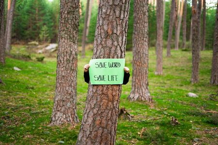 Teenager holding a banner around a tree in the woods. Save world, the life. Concept of sustainability.の写真素材