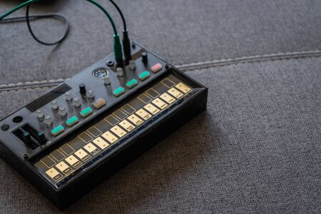 Close up view of small black fm synthesizer with patch cable on top of a sofa with space to the...