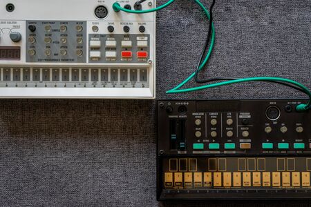 Top view of black fm synthesizer and a white sampler drum box with patch cables with a gray textured...