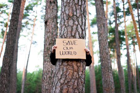Low view of a teenage activist holding banner around a tree with a environmental message. Save our world. Concept sustainability.の写真素材