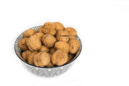 Top view on heaps of walnuts in black and white design bowl on white studio background