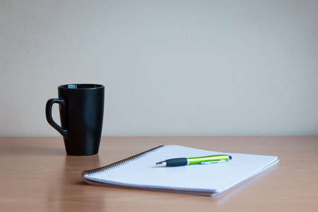 Cup, pen and a notebook in a wooden table.