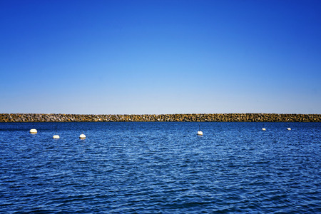 Stone breakwater on the horizon at the Baltic Sea under a blue sky.