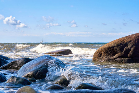 Big stone in the Baltic Sea. With sailboat in the background.の写真素材