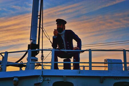 Sailor figure sits on the deck of a boat. With sunset in the background.の写真素材