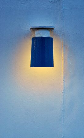The blue lamp shines with warm light on the white wall.の写真素材