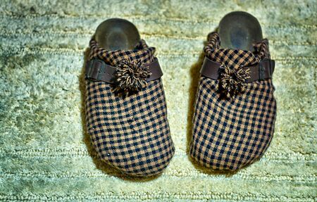 Old plaid worn slippers on an old carpet.