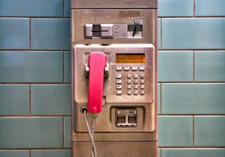 Public telephone made of silver metal with pink telephone receiver.の写真素材