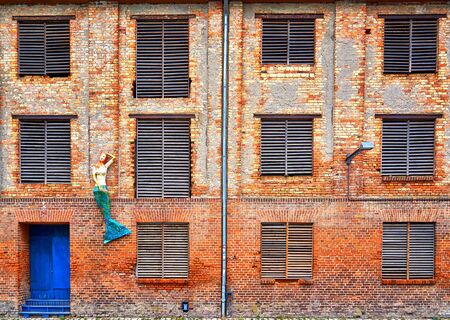 Mermaid at the facade of an old industrial brick building with old door and windows. Old town of Stralsund in Germany.の写真素材