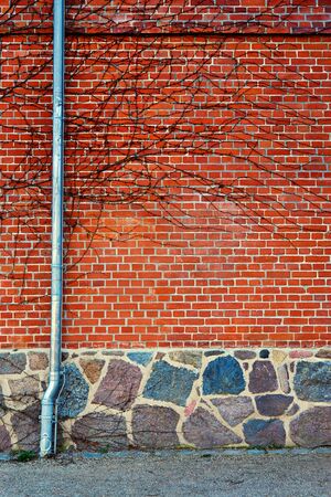 Downpipe on a red brick wall with natural stone foundation.の写真素材