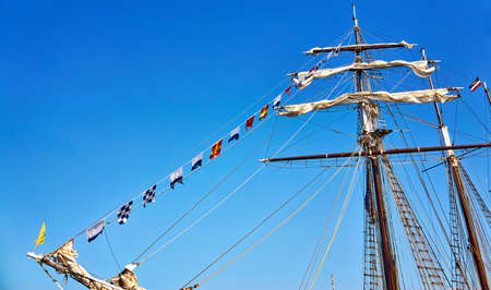International maritime signal flags on a flagpole on a sailing ship with a blue sky in the...