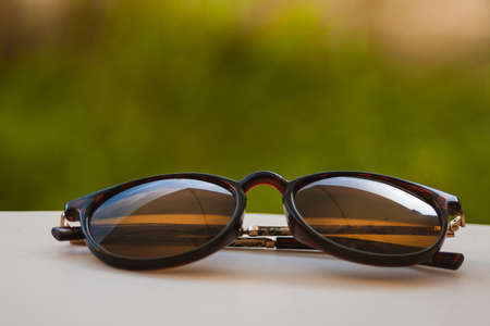 Brown sunglasses leaning against a white table with grass background in warm tones.