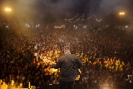 young rock musician on stage playing guitar Young rock musician on stage playing the guitar with the background of all the fans.の写真素材