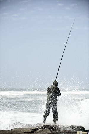 Young man fishing at sunset on a pier in front of the seaの写真素材
