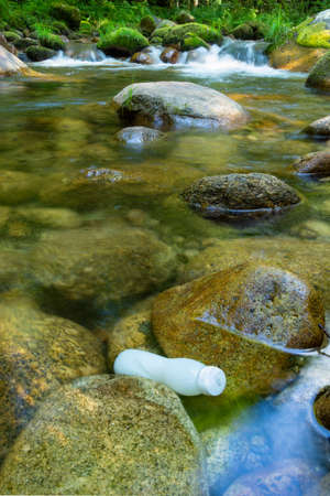 Plastic bottle pollution in forest stream. Rocks with moss and green vegetation.の写真素材