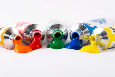 Gouache tube dripping orange, red, green, blue and yellow paint. White backgroundの写真素材