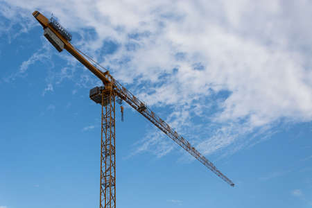 Yellow tall construction crane. Blue sky and white clouds