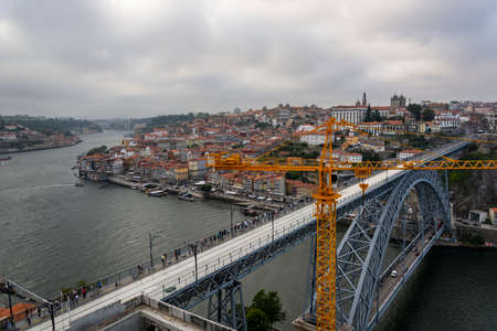 View to thef old Porto city: yellow construction crane and D. Luis bridge made of iron. Douro river with a boat.のeditorial素材