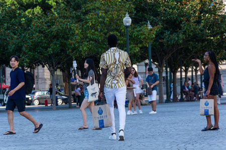 Porto, Portugal - 08/28/2019: African stylish man walking, wearing white pants and a white shirt with golden stripes. Crowd of people.のeditorial素材