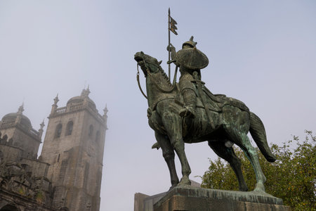 Statue of a medieval warrior (knight ) on his horse in the foreground and cathedral in the background. Knight VÃ­mara Peres and Porto Cathedral. Foggy day. Porto, Portugal.の写真素材