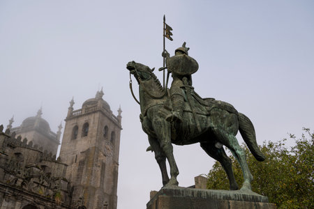 Statue of a medieval warrior (knight ) on his horse in the foreground and cathedral in the background. Knight VÃ­mara Peres and Porto Cathedral. Foggy day. Porto, Portugal.の写真素材