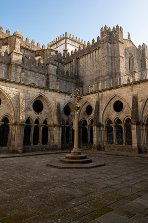 Porto cathedral seen from the inner courtyard. Old cross made of stone in the middle. Building made of stone Blue sky. Porto, Portugal.の写真素材