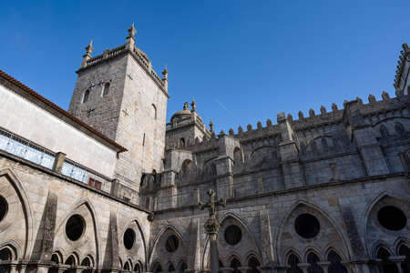Porto cathedral seen from the inner courtyard. Old cross made of stone in the middle. Building made of stone Blue sky. Porto, Portugal.のeditorial素材
