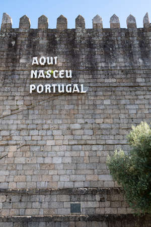 Medieval wall with the words âHere Portugal has bornâ. Tree in the foreground. Blue sky. GuimarÃ£es, Portugal.のeditorial素材