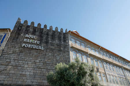 Medieval wall with the words âHere Portugal has bornâ. Tree in the foreground. Blue sky. GuimarÃ£es, Portugal.のeditorial素材