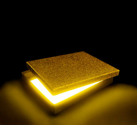 Golden color gift box. Opened box against black background with copy space. Fantasy light effect inside.の写真素材