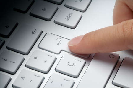 Index finger pressing enter key at keyboard. Fade light effect on keyboard.