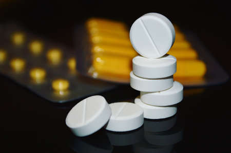 White pills staked and yellow capsules in background    の写真素材