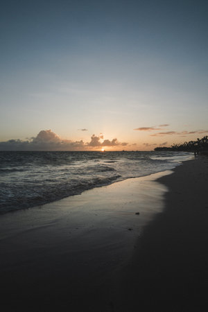 Gentle waves lap at the shore as the sun sets on the horizon, casting warm colors across the sky....