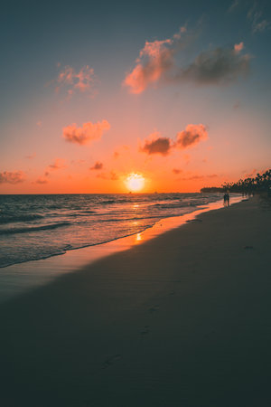 Soft waves lap against the shore as the sun sets, casting warm colors across the sky. Silhouettes of...