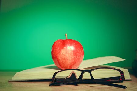 view of open book  with reading glasses and apple on wooden tableの写真素材
