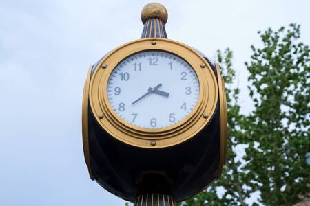 Circle street clock on a blue sky and green tree background. の写真素材