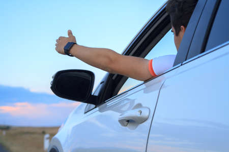 Man in the car on her summer vacation and road trip waving hand out of the window.の写真素材