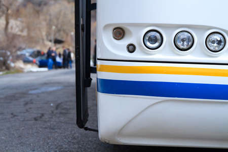 White bus on parking frontally close up with group of tourists background. 
