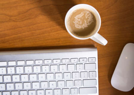 Office desk table with computer keyboard and coffee cup on desk.